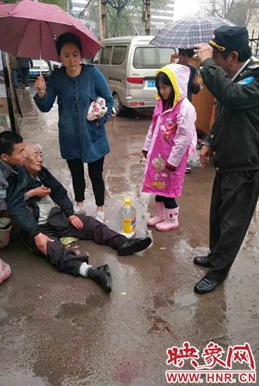 女孩為倒地老人撐傘。 女孩為倒地老人撐傘。