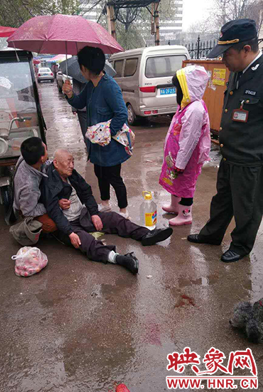 女孩為倒地老人撐傘。 女孩為倒地老人撐傘。