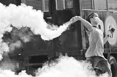 12月2日，泰國曼谷，一名反政府示威者在總理府附近向負責執勤的警察投擲催淚彈。英拉請求示威者不要再試圖占領政府工作部門，不要逼迫政府工作人員選邊站。