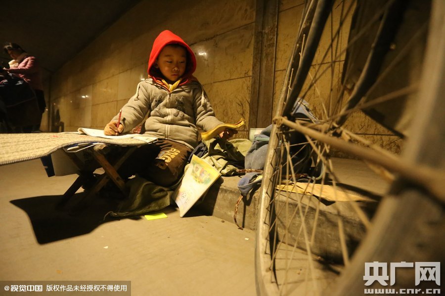 2015年11月8日晚，鄭州，7歲男孩涵洞橋下陪父母練攤，路邊燈下坐小馬扎上寫作業(yè)。