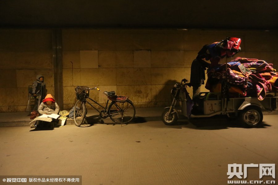 2015年11月8日晚，鄭州，7歲男孩涵洞橋下陪父母練攤，路邊燈下坐小馬扎上寫作業(yè)。